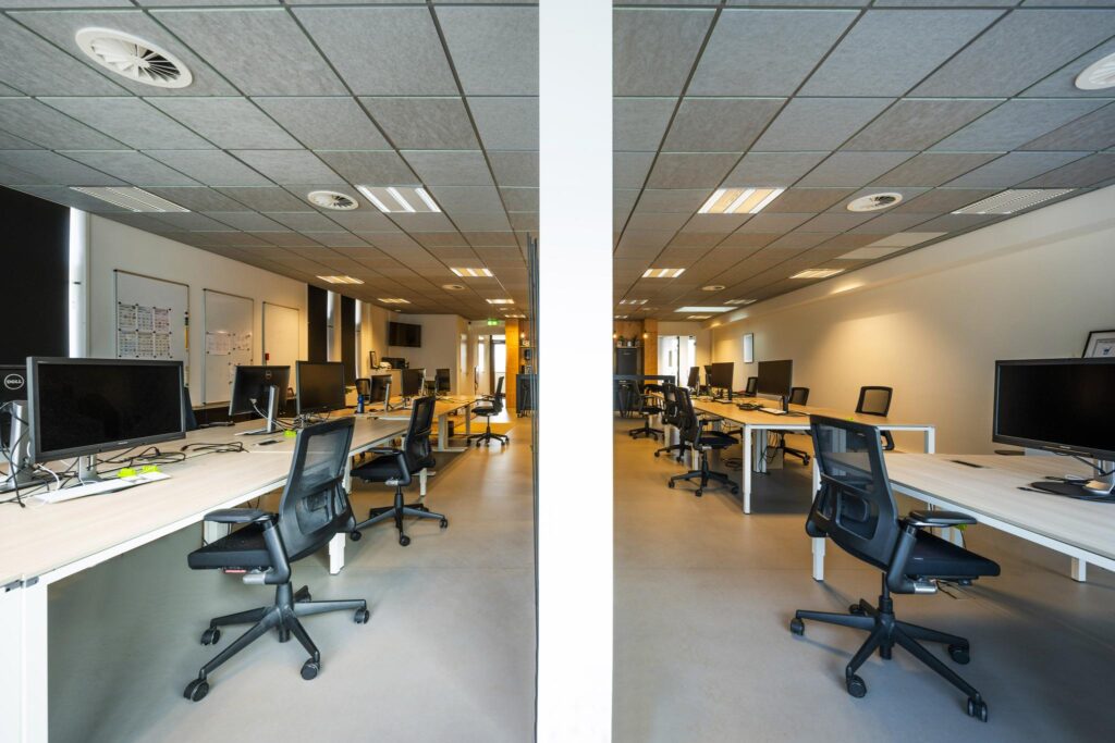 Moderne en ruime kantoorruimte aan de De Ruijterkade met werkplekken en computerschermen aan lange bureaus.